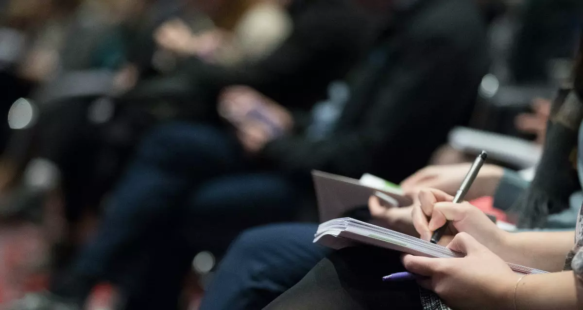 Menschen sitzen nebeneinander, nehmen zum Teil Notizen.