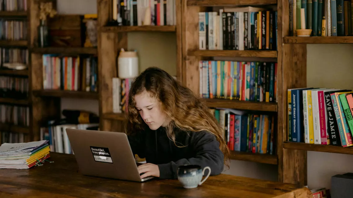 Ein Mädchen sitzt mit einem Laptop vor einem Bücherregal