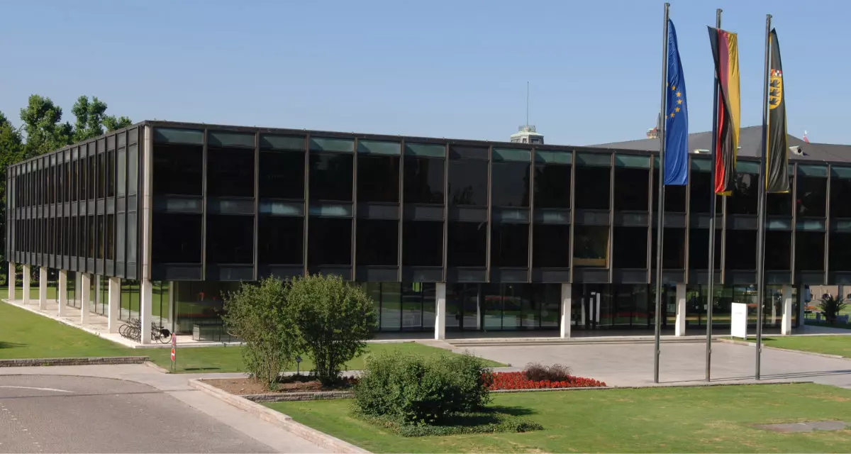 Vorderansicht des Landtags von Baden-Württemberg mit Europa-, Deutschland- und Landesflagge.